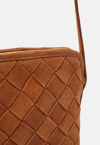 Hnědá semišová kabelka s tkaným diamantovým vzorem, s horním zipovým uzávěrem a jedním popruhem na rameno.
