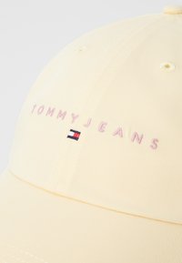 Žltá baseballová čiapka vyrobená z bavlny s vyšitým nápisom "TOMMYJEANS" v ružovej farbe a malou nášivkou loga v červenej, bielej a modrej farbe.