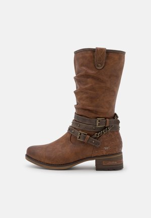 Keskipitkässä ruskeassa nahkasaappaassa on koristeelliset hihnat, soljet, ketjuyksityiskohta, matala pino korko ja kantapään alueella kohokuvioitu kukkakuvio.