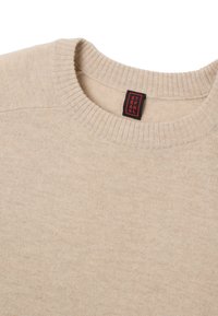 Beige gebreide trui met een kabels ribbelkraag en een zachte textuur. Voorzien van een zwart en rode label met de tekst "STANLEY".