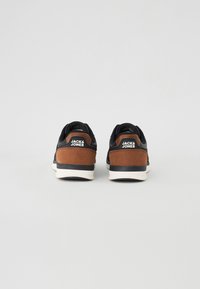 Black and brown suede sneakers with white soles, featuring branding on the heel and a textured finish. Classic athletic design.
