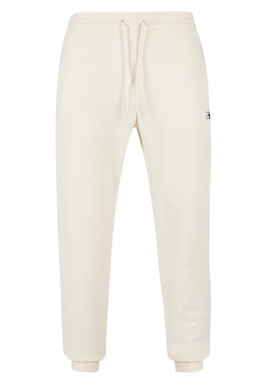 Krémové jogger nohavice vyrobené z mäkkého materiálu, s elastickým pásom na šnúrku, manžetami na nohaviciach a malým logom na boku.