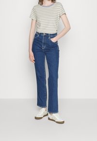 Randig t-shirt med kort ärm och lavendelfärgad krage, i kombination med högmidjade blå denimjeans. Modellen har på sig vita sneakers med beige detaljer.