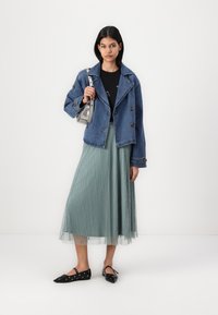 Denim jakna z velikimi gumbi, črna majica, nabrana krila v mentol zeleni barvi in črne balerinke z očesci. Srebro torbica dopolnjuje outfit.