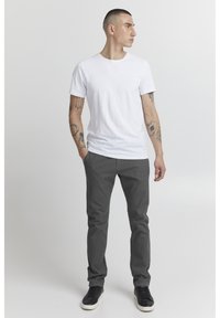 Vit bomullströja med rund hals, ihop med mörkgrå slim-fit-byxor och svarta sneakers, med en slät yta och minimalistisk design.
