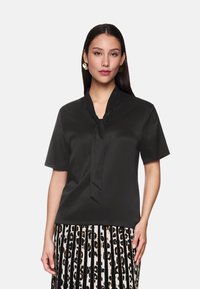 Schwarze Kurzarmbluse mit einer Schleifenkragen, aus einem glatten Stoff gefertigt. Kombiniert mit einem gestreiften Rock in Schwarz und Weiß mit einem Leopardenmuster.