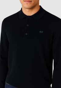 Polo a maniche lunghe nero con colletto, tre bottoni e un logo ricamato blu sul petto. Tessuto dalla trama liscia.