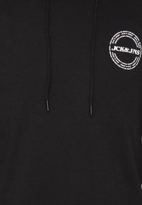 Zwarte hoodie gemaakt van zacht stof met een ronde grafische logo in het wit op de borst en zwarte koorden met plastic tips.
