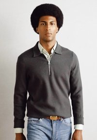 Maglione a collo zip in misto lana grigio scuro. Abbinato a una camicia collare verde chiaro e jeans in denim blu.