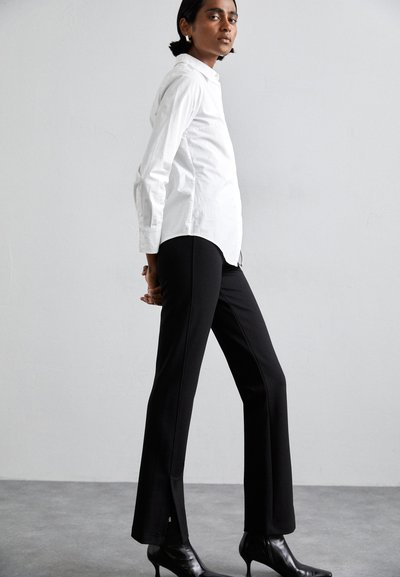 White button-up shirt with a structured collar and long sleeves, paired with black flared pants and pointed black heels.