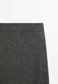 Section de tissu tricoté côtelé gris foncé avec un bord droit, probablement une partie d'un vêtement sur fond blanc.