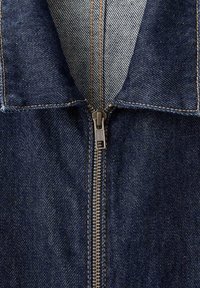 Veste en denim avec un tissu bleu foncé, présentant un détail de fermeture éclair vertical au centre et une doublure intérieure contrastante avec un motif bleu clair.
