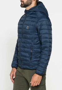 Giubbotto imbottito blu navy con cappuccio, caratterizzato da sezioni trapuntate, chiusura con zip frontale e tasche laterali. Design testurizzato, leggero e aderente.