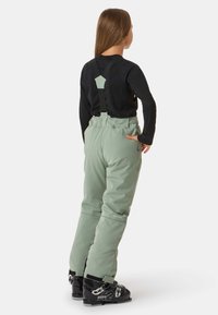 Mintgrüne Skihosen mit verstellbaren schwarzen Trägern, einer hohen Taille und einer glatten Textur. Kombiniert mit schwarzen Skischuhen mit weißen Grafiken.