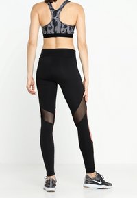 Leggings deportivos negros con paneles de malla y un acento rosa en el lateral. El diseño incluye una cintura alta y un corte hasta el tobillo.