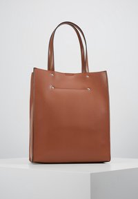 Brązowa prostokątna torba na ramię o gładkiej fakturze, wyposażona w dwa długie uchwyty oraz dwa ozdobne srebrne nity na przedniej stronie.