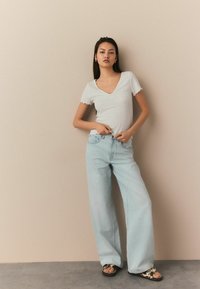 Haut ajusté gris clair avec des manches à vagues, associé à un jean large bleu clair taille haute et des sandales à motifs. Design simple et décontracté.