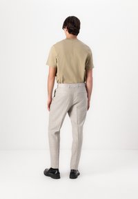 Beige kortärmad skjorta, ljusgrå rutiga byxor och svarta skor. Enkel, ren design med minimal detaljering.