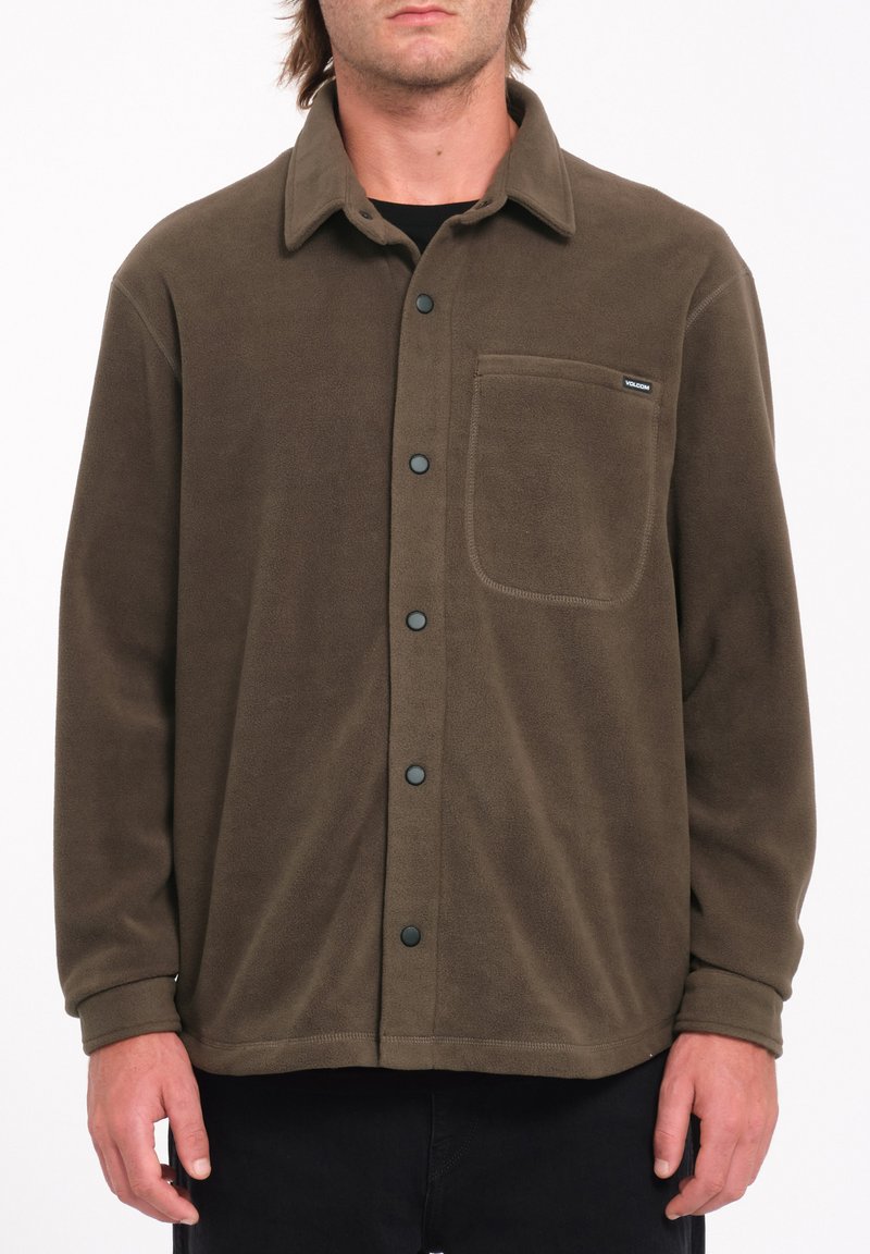 Veste en polaire marron avec un devant à boutons, un col et une poche poitrine. Équipée de boutons pression noirs et d'une texture lisse.