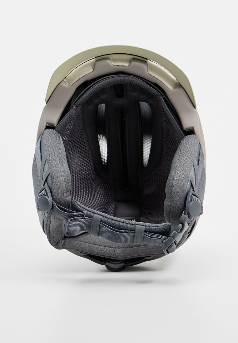 Szary kask o gładkiej powierzchni z matowym akcentem w oliwkowym zielonym kolorze. Wnętrze zawiera siatkę podszewkową oraz regulowane paski dla bezpiecznego dopasowania.