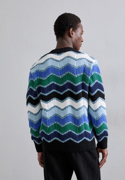 Knit sweater featuring a zigzag pattern in blue, green, black, and white. Finished with a ribbed collar and cuffs, textured yarn detail.