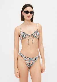 Blommig bikini-set med knyt-fram bralette och matchande låga byxor, med pastellfärger, små axelband och en slät tygkvalitet.