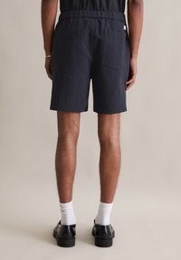 Marineblauwe shorts van textuurstof, met een elastische tailleband en een achterzak. Gecombineerd met witte sokken en zwarte schoenen.