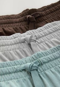 Drie paren rekbare shorts met elastische tailleband in bruin, grijs en lichtblauw, met geknoopte strikken en een zachte stoftextuur.