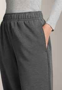 Szürke sportnadrág rugalmas derékpánttal, oldalzsebekkel és sima, texturált anyagból. Közeli kép, amely a laza illeszkedést mutatja.