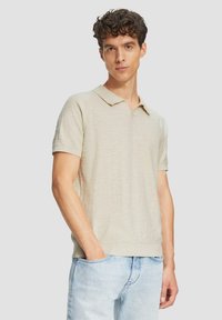 Beige polo shirt met korte mouwen en een kraag, met een gestructureerd breipatroon en ribgebreide manchetten, gedragen met lichtblauwe spijkerbroek.