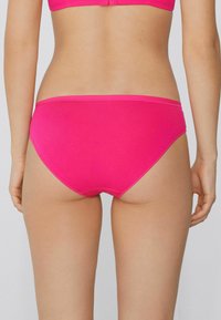 Růžové bavlněné tanga s hladkou texturou, s jednoduchým designem a středním střihem, doplněná kontrastním pasem.