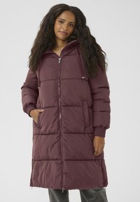 Cappotto puffo lungo color bordeaux con chiusura a zip, cappuccio, polsini a coste e tasche laterali. Presenta un design trapuntato e una texture liscia.