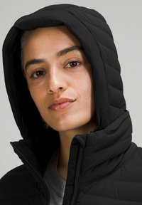 Zwarte gewatteerde jas met een ritssluiting aan de voorkant en een capuchon, voorzien van een geplooide textuur en een hoge kraag voor extra warmte.