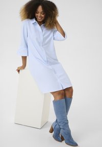 Abito camicia a righe blu e bianche con chiusura a bottoni e maniche a tre quarti, abbinato a stivali in camoscio azzurro chiaro e con una finitura testurizzata.