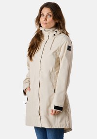 Giacca impermeabile beige con cappuccio, dotata di tasche con cerniera, taglio dritto e polsini regolabili con accenti neri.
