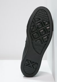 Semelle de chaussure en caoutchouc noir avec motif de grip texturé, présentant un design en losange et le logo Converse All Star. Côtés lisses et bords arrondis.