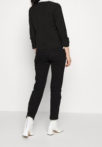 Černý přiléhavý top s dlouhými rukávy, kombinovaný s černými skinny džíny. Bílé kotníkové boty na blokovém podpatku se stříbrným zipem vzadu.