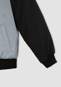 Bomber bunda ve stylu color-block s rukávem v světle šedé barvě a černým tělem, která má žebrovaný manžet a boční kapsu orámovanou stehem.