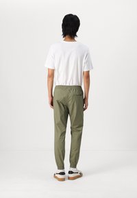 Witte T-shirt gecombineerd met olijfgroene tapered broek met een elastische tailleband en omslagmanchetten. Klassieke sneakers maken de outfit compleet.