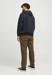 Navy hoodie with a drawstring hood, paired with brown cargo pants featuring side pockets and black sneakers with white soles.