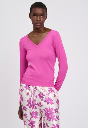 Roze lange mouwen V-hals trui gemaakt van zachte stof. Heeft een getailleerd ontwerp en geribbelde zoom, gecombineerd met witte broek versierd met roze bloemmotieven.