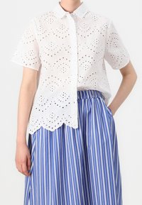 White short-sleeved shirt featuring cut-out embroidery and scalloped hem, paired with a blue and white striped skirt with an elastic waistband.