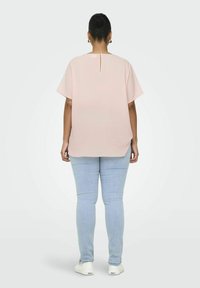 Jasnoróżowa bluzka z krótkimi rękawami, z otworem w tylnej części, zestawiona z jasnoniebieskimi, dopasowanymi dżinsami i białymi trampkami.
