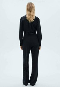 Svart skräddarsydd jumpsuit med långa ärmar, midjebälte och vida byxor. Slät tyg med en ren, minimalistisk design.