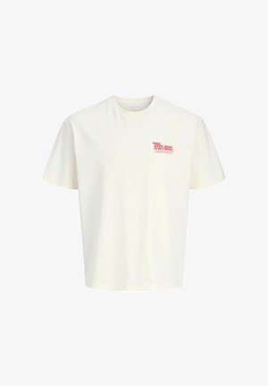 Luźna jasnobeżowa koszulka z czerwonym logo, w zestawieniu z oversize'owymi szarymi spodniami i białymi sneakersami. Swobodny, zrelaksowany strój.