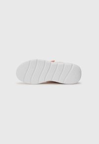 Semelle de chaussures en caoutchouc blanche avec des stries texturées pour l'adhérence, présentant une surface lisse et une subtile empreinte de logo près du talon.