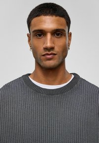 Pull en tricot côtelé gris avec un col rond, superposé à une chemise blanche à col rond, sans motifs visibles, tissu texturé.