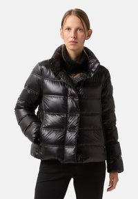Schwarze Pufferjacke mit glänzender Textur, verkürzter Länge, hohem Kragen und diagonaler Naht. Verfügt über verdeckte Knöpfe und Seitentaschen.