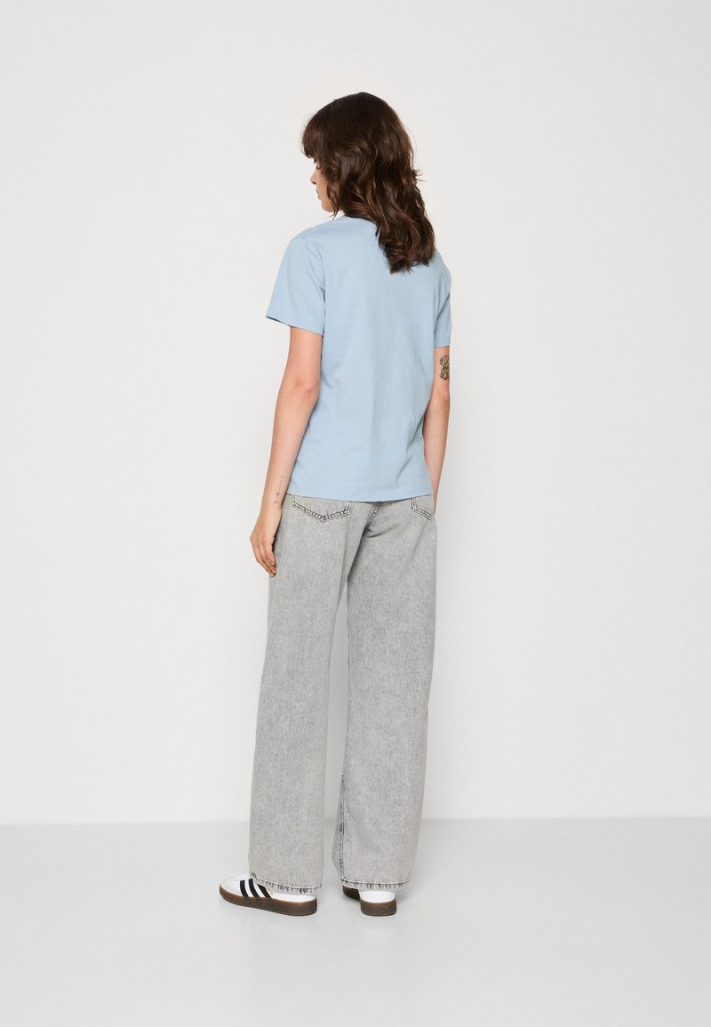 Ljusblå t-shirt, kortärmad, figurnära design; kombinerad med löst sittande grå denimbyxor med fransar vid fållen och subtila detaljer.