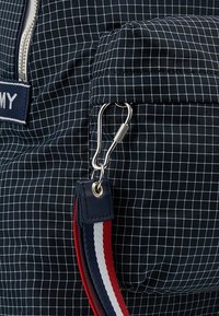 Marinfärgad tygväska med vitt rutmönster, utrustad med dragkedja, en silverklämma och ett texturerat band med röd, vit och blå accent.